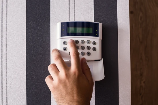 Intérieur résidentiel, main masculine saisissant un clavier de système d'alarme mural blanc
