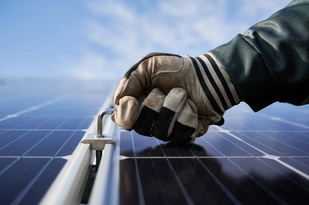 Ouvrier installant des panneaux solaires photovoltaïques sur toiture résidentielle, portant équipement de sécurité, ciel bleu dégagé