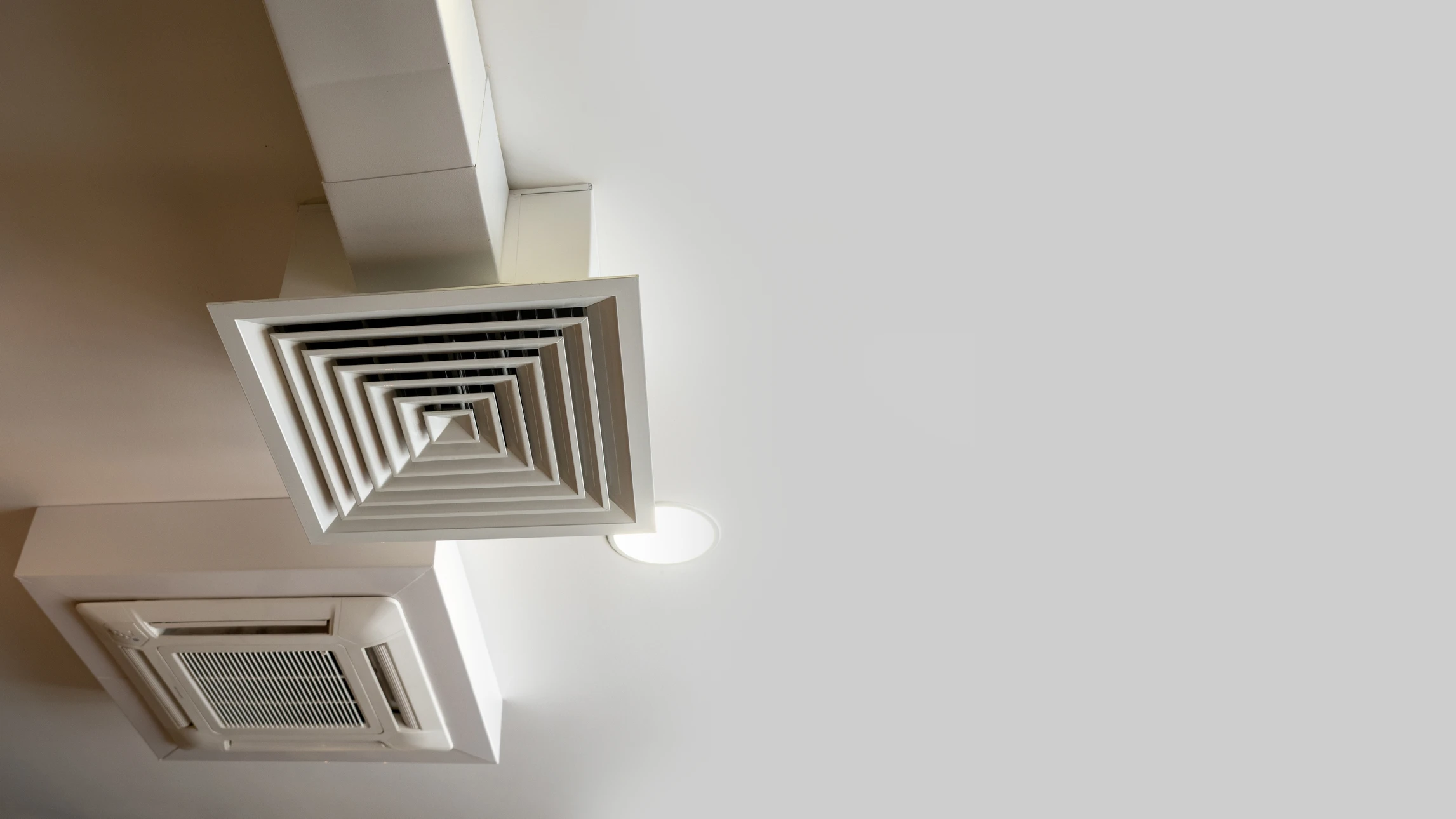 Technicien en combinaison beige avec bandes bleues et rouges installant une grille de ventilation au plafond dans un intérieur résidentiel