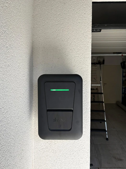 Électricien en salopette bleue et chemise à carreaux consulte un schéma technique devant un tableau électrique ouvert