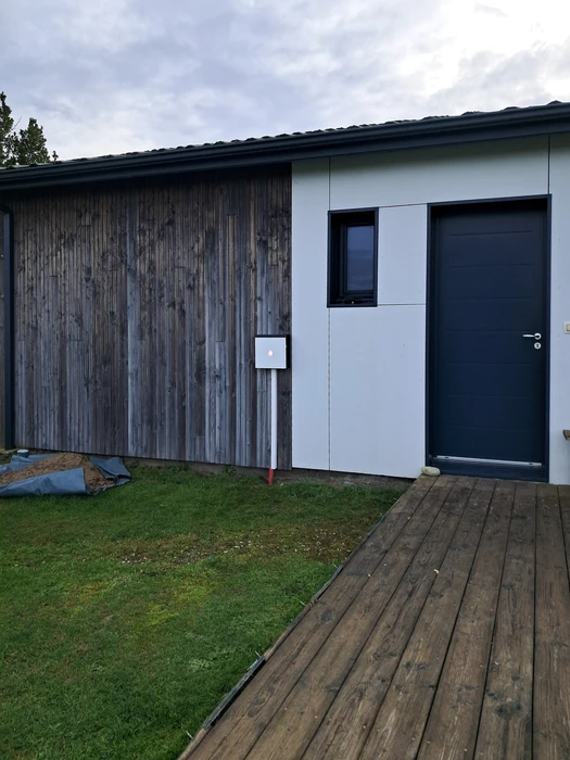 Un électricien professionnel en salopette bleue et casquette installe un tableau électrique dans un bâtiment en construction